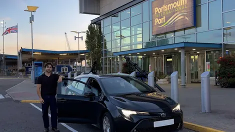 Bobby, Navigo's owner and driver, by the open door of the black Toyota Corolla estate outside Portsmouth International Port.